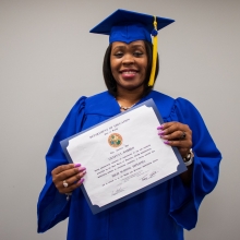 Geneva Barber in a cap and gown, holding her diploma