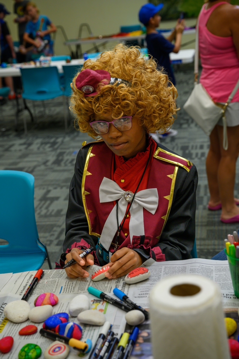 A young girl in cosplay paints rocks in the community room